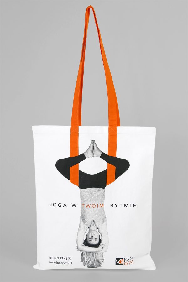 Biała, bawełniana torba z widoczną kobietą w pozycji joga, widoczny napis Joga w twoim rytmie z pomarańczowymi uszami wszytymi w torbę